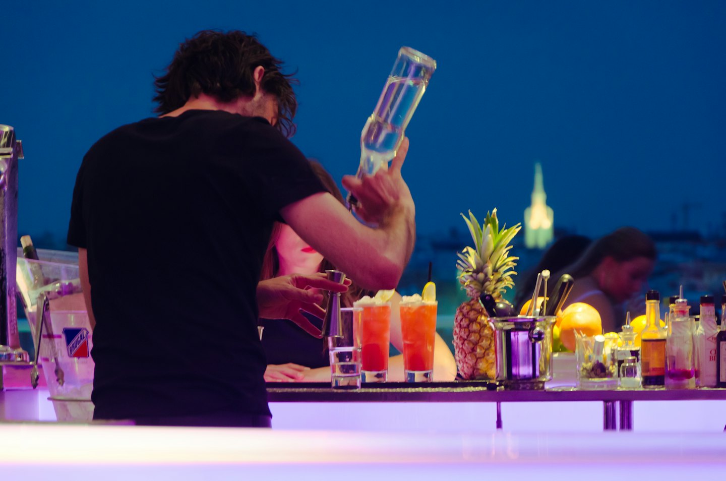 Bartender pours a drink at an outdoor bar at night.