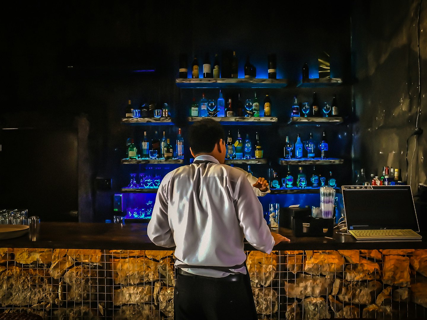 Bartender mixing drinks behind a backlit bar counter.