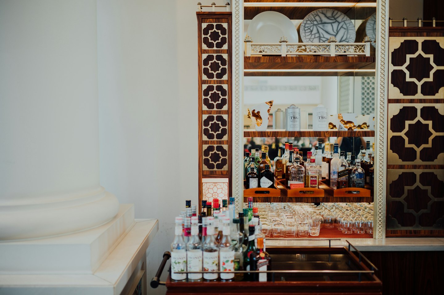 An elegant bar cart sits beside a geometric mirrored cabinet.